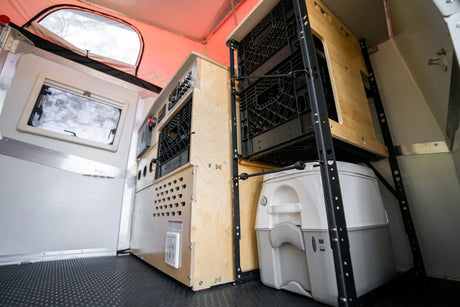 Inside this rv rental: portable toilet, black crate storage, and control panel, ideal for off-grid travel.