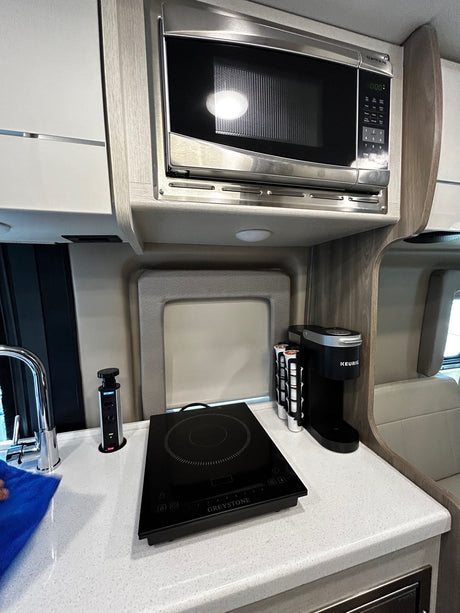 Well-equipped RV rental kitchen: microwave, induction cooktop, Keurig coffee maker, and pop-up counter outlets.