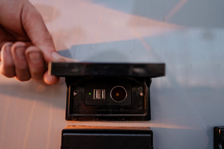 A hand opens an RV power outlet showing USB and 12V ports, vital for charging devices on your rv rental trip.