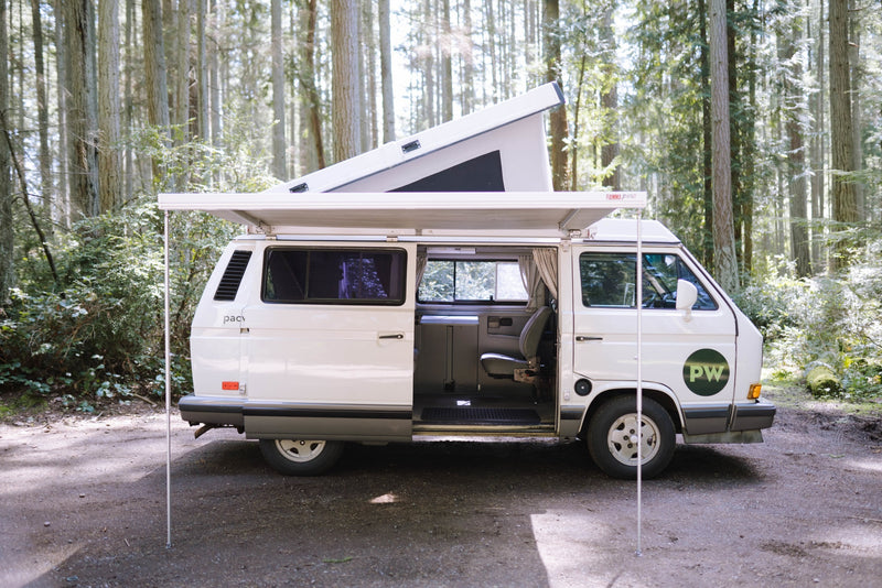  bathed in golden light.|White pop-top camper van (RV rental) with awning extended — photo 2