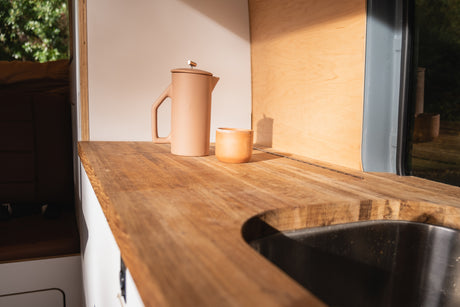 RV rental kitchen detail: light wood countertop, sink, and a matching coffee pot with cup.