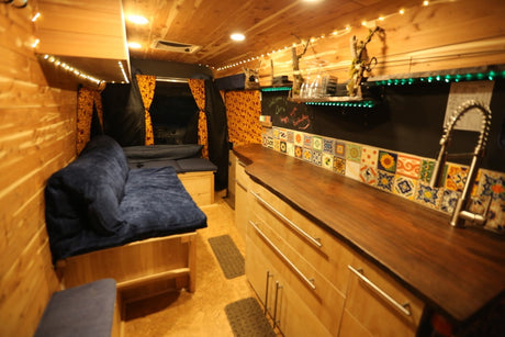 Cozy rv rental interior with wooden walls, a blue futon, and a kitchen area with a tiled backsplash.