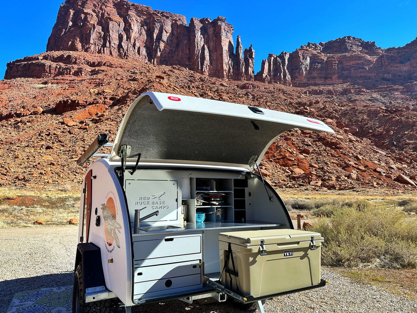 Experience the desert with this RV rental! A teardrop camper's open rear reveals a sleek outdoor kitchen & Yeti cooler against red rocks. — photo 9