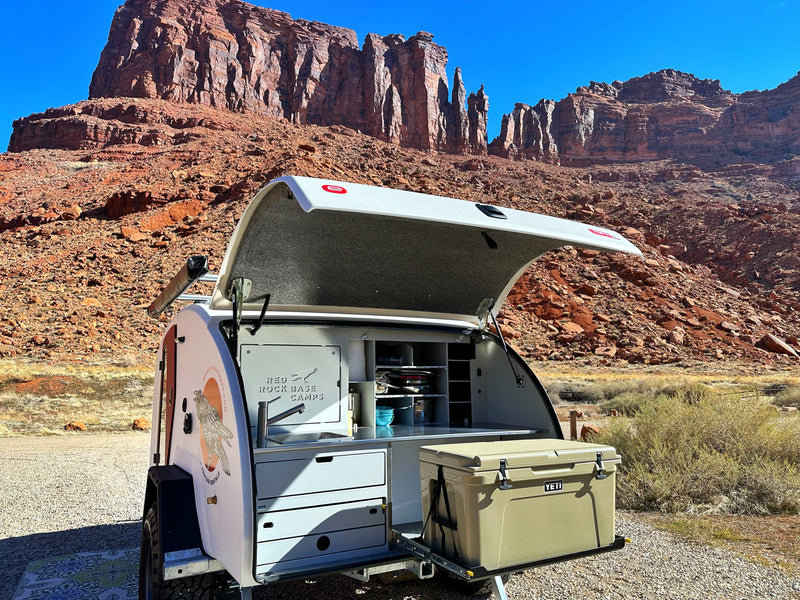 Experience the desert with this RV rental! A teardrop camper's open rear reveals a sleek outdoor kitchen & Yeti cooler against red rocks. — photo 9
