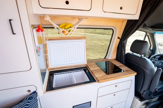  and the van's driver cabin visible.|RV rental kitchen setup: Open drawer reveals compact — photo 6