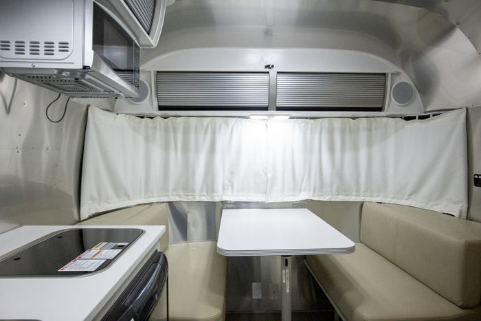 Cozy RV rental interior showing kitchen cooktop, microwave, and a bright dining space with white table and beige benches.