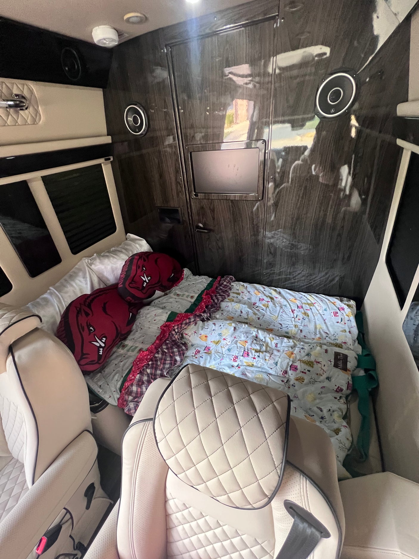 Inside a luxury rv rental: cream leather seats, dark wood walls, bed with Razorback pillows, and entertainment.