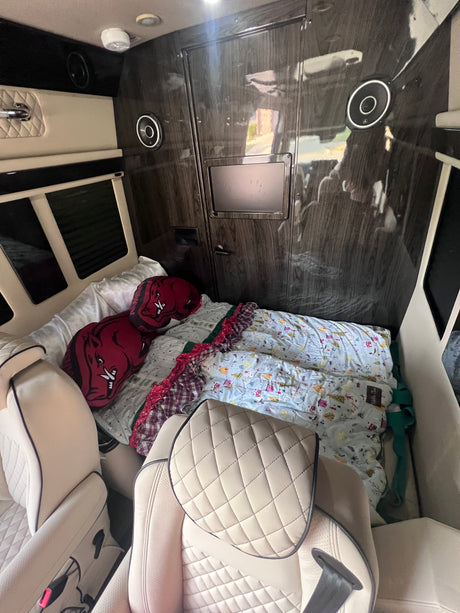 Inside a luxury rv rental: cream leather seats, dark wood walls, bed with Razorback pillows, and entertainment.