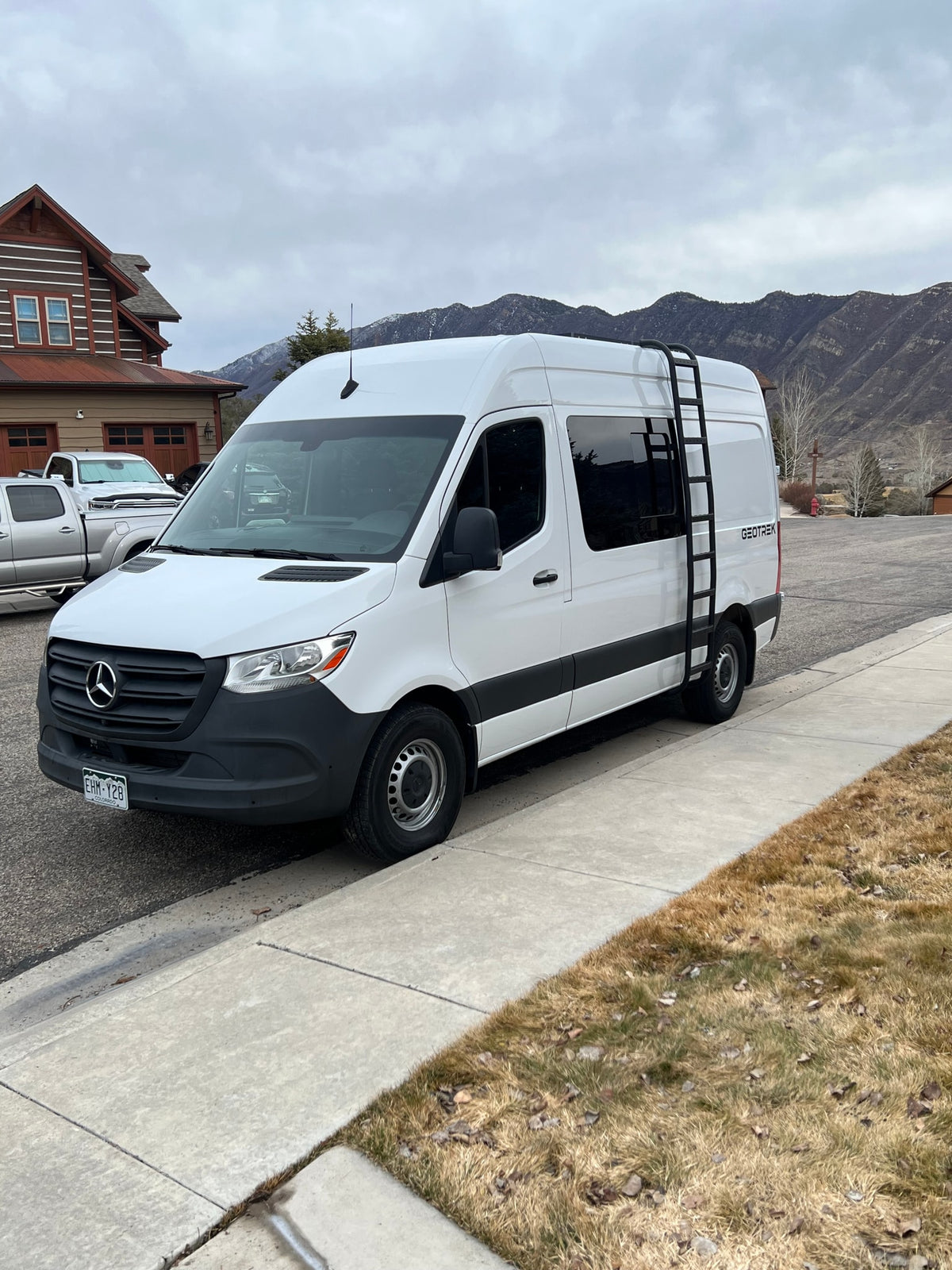 White Mercedes-Benz Sprinter van by GEOTREK, likely an RV rental, parked roadside with mountains in view. — photo 7