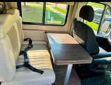 Inside an rv rental: a dining area with a light bench seat, black seatbelt, and a dark table beside a swivel front seat.