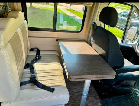 Inside an rv rental: a dining area with a light bench seat, black seatbelt, and a dark table beside a swivel front seat.