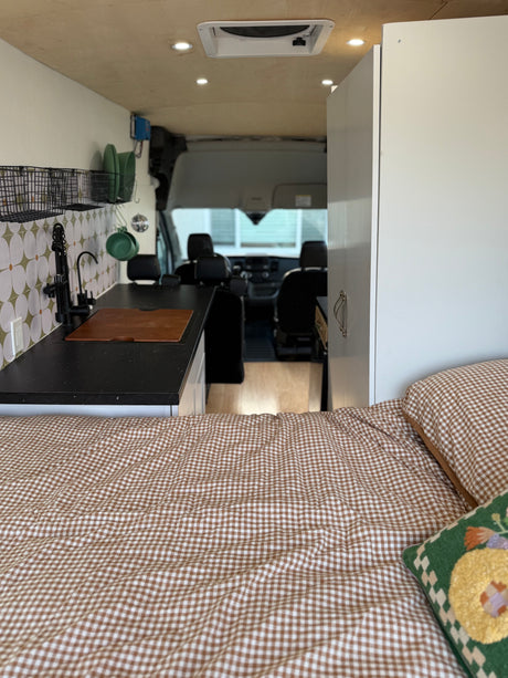 Cozy RV rental interior featuring a gingham bed, modern kitchen with a sink & backsplash, and a view into the front cabin.