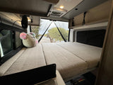 Relaxing RV rental interior with a spacious bed, plush toy, and rear window view. Perfect for camper van adventures.