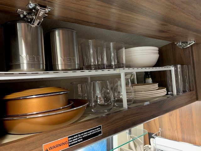 Optimized kitchen storage inside an RV rental cabinet, featuring clear glasses, Yeti tumblers, stacked dishes & pans using a shelf organizer. — photo 12