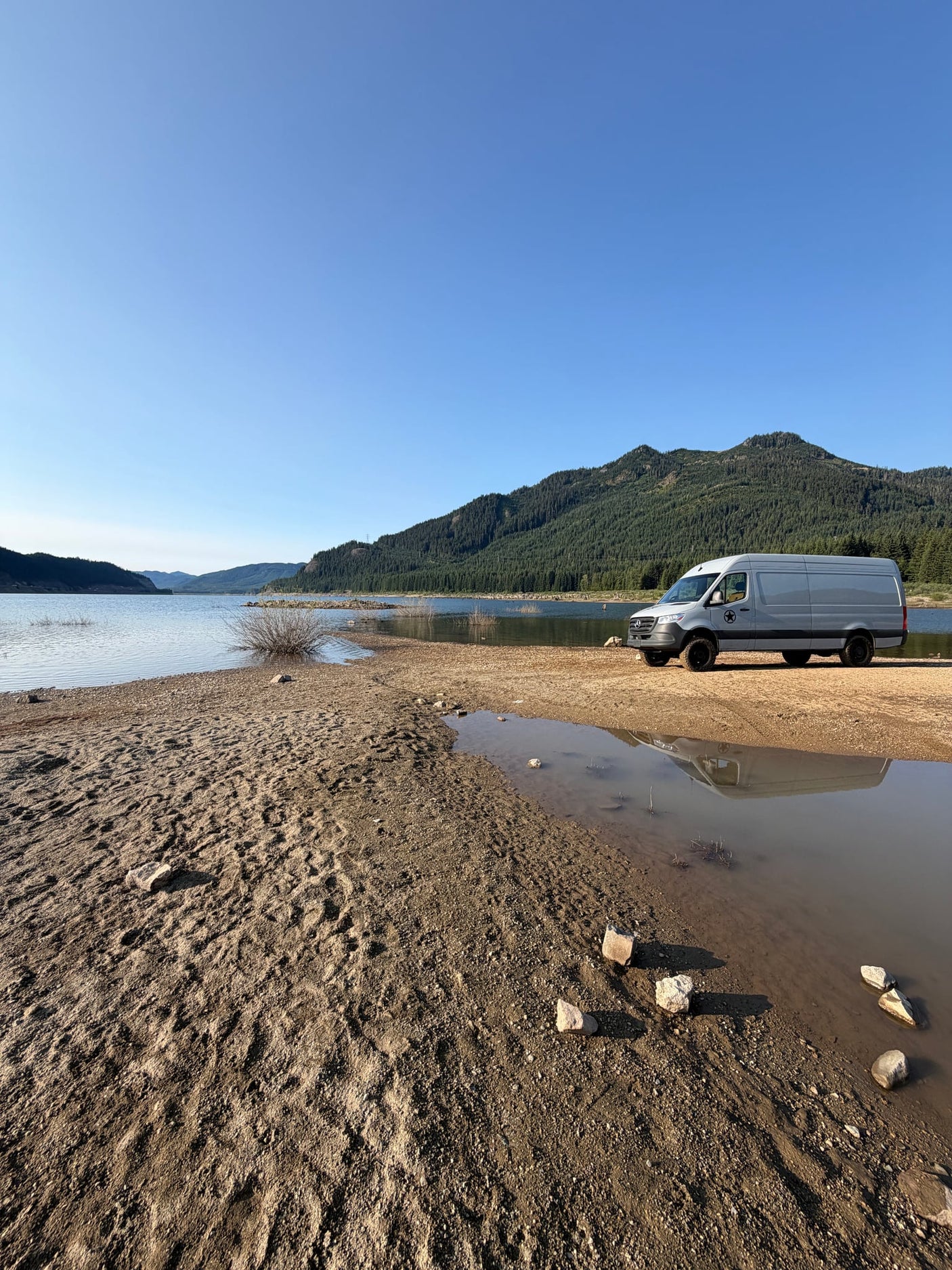  parked on a beach by a lake and mountains. Great RV rental for adventure.|For RV rental: This AWD 170 camper van offers a bed