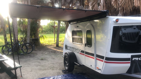 Teardrop rv rental at a sunny campsite with bikes and a picnic table, perfect for outdoor camping adventures.