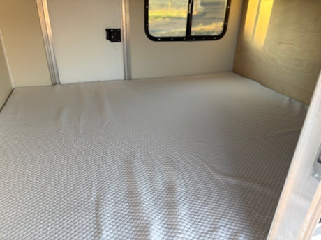 Interior of an RV rental: a large, light-colored quilted mattress creates a cozy sleeping area.