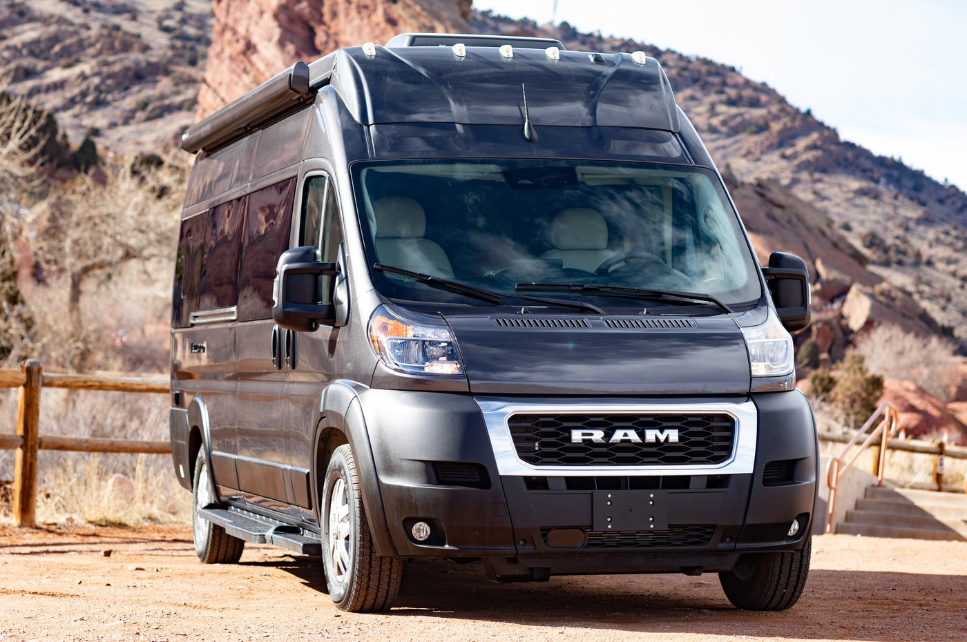  ideal for your next RV rental adventure. Parked against stunning red rock scenery.|Front view of a black Ram ProMaster RV rental — photo 6