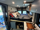 This RV rental's cozy interior features a full bed, modern lighting, and a small sink area, ideal for travel.