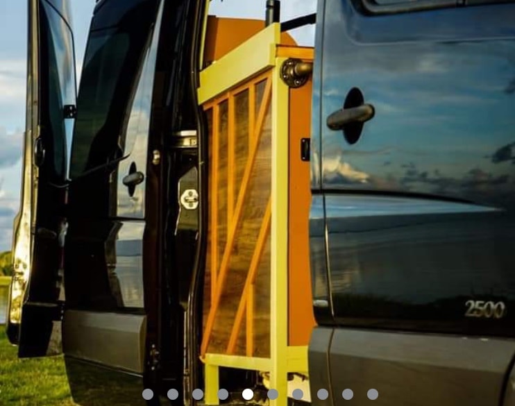  clouds reflecting in windows.|Open rear doors of a dark Mercedes Sprinter 2500 RV rental expose a warm custom-built wooden interior.|Cozy RV rental interior: wooden cubbies — photo 3