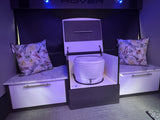 RV rental: Compact interior with a white portable toilet, flanked by storage benches with patterned pillows.