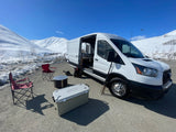 RV rental campervan set up for adventure in snowy mountains, featuring outdoor chairs, cooler, and a drone.