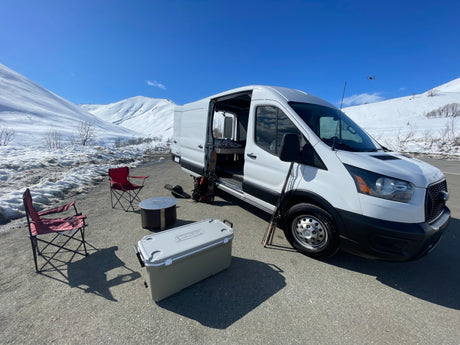 RV rental campervan set up for adventure in snowy mountains, featuring outdoor chairs, cooler, and a drone.