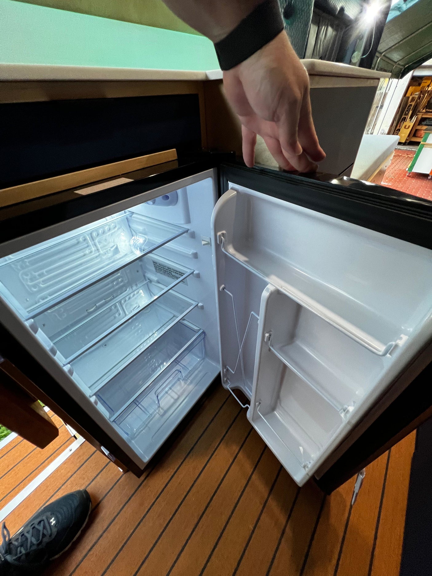 Empty mini-fridge in an rv rental, shelves & door storage visible. Hand opens it, ready for compact travel essentials.