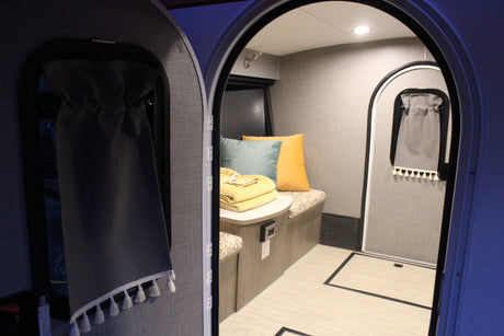 Inside a modern RV rental, a compact living space is visible through arched doorways, featuring a bench, table, and soft furnishings.