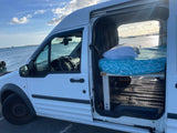 White camper van by the ocean with its side door open, revealing a bed inside. Perfect for an RV rental adventure.