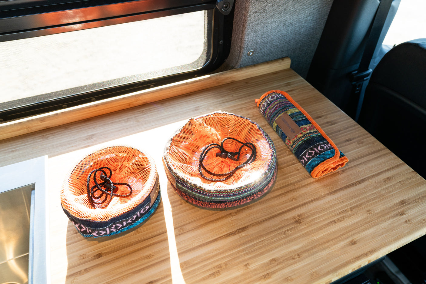 RV rental: Organized bamboo counter with two mesh bags and a colorful rolled item beside a sunny window.