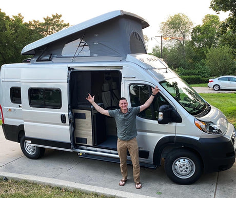 Happy man shows off his silver Solis rv rental camper van with an extended pop-top roof. The side door is open, revealing the interior.