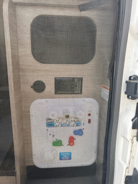 RV rental utility panel with water connections, valves, and controls visible behind a protective mesh screen.