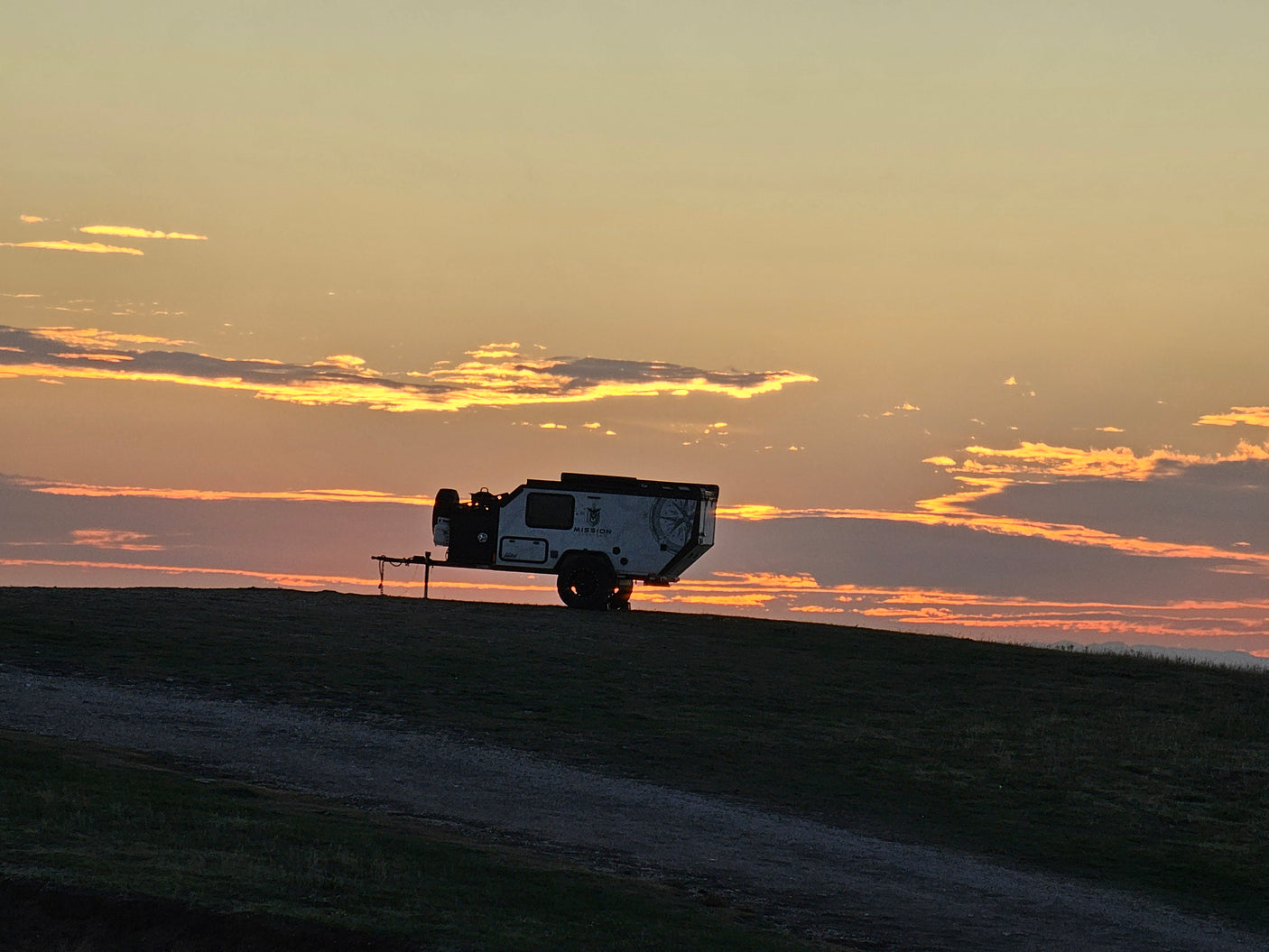 An off-road camper trailer, silhouetted on a hill against a fiery sunset with vibrant clouds. Your ideal rv rental for camping.
