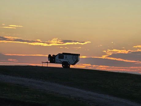 An off-road camper trailer, silhouetted on a hill against a fiery sunset with vibrant clouds. Your ideal rv rental for camping.