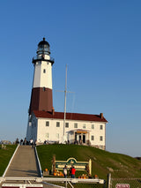Tall Montauk Point Lighthouse & keeper's house on a hill, clear sky. Ideal for an RV rental trip to this historic destination!