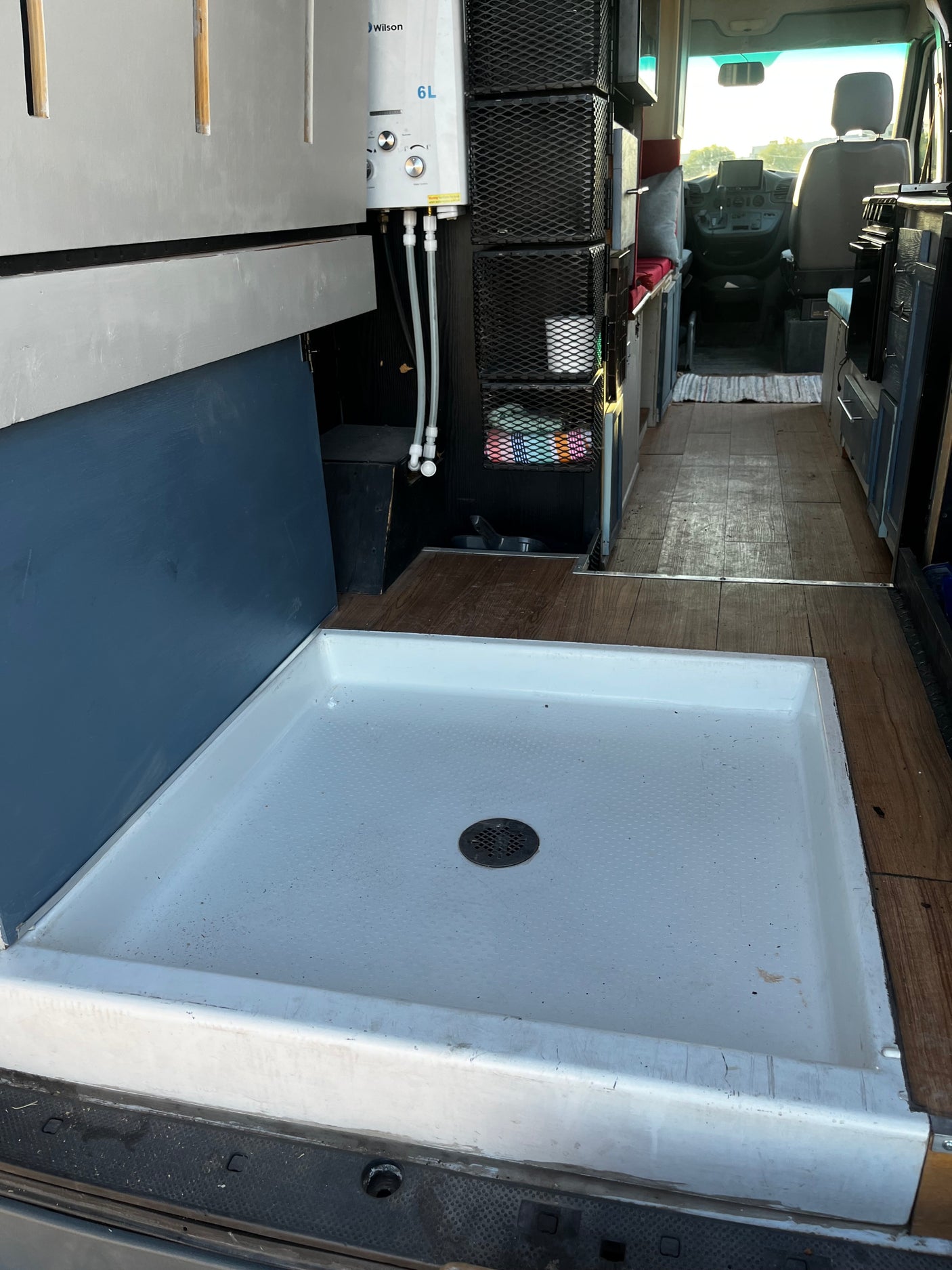 RV rental: Camper van interior showing a white shower pan with drain, "Wilson 6L" water heater, and mesh storage.