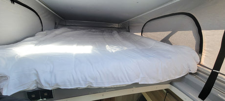 Bright and cozy pop-top bed with white comforter inside an RV rental, ready for comfortable travel adventures.
