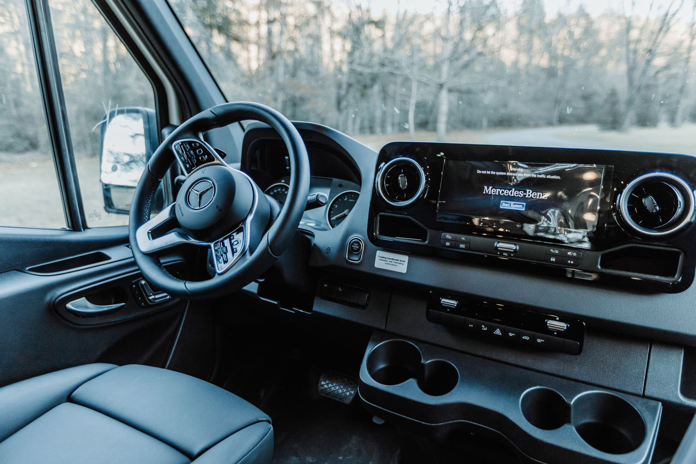 Inside a Mercedes-Benz RV rental: a clean, modern dashboard with steering wheel and large display. Road visible ahead.
