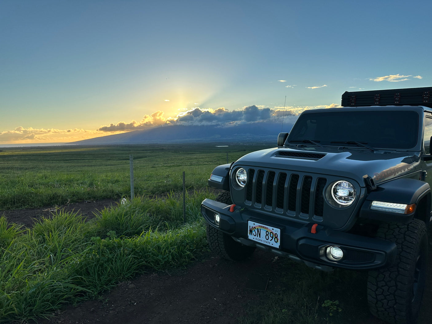 Jeep Wrangler with rooftop tent at sunset in Hawaii, offering beautiful field & mountain views. Ideal RV rental.