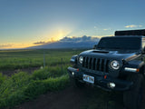 Jeep Wrangler with rooftop tent at sunset in Hawaii, offering beautiful field & mountain views. Ideal RV rental.