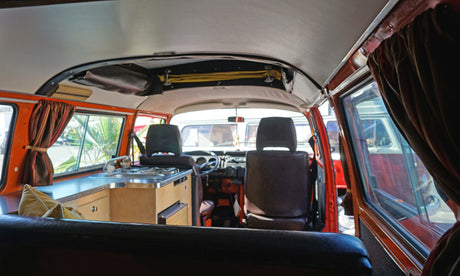Inside a classic orange camper van, featuring a compact kitchen, front seats, and curtains. Ideal RV rental for trips.