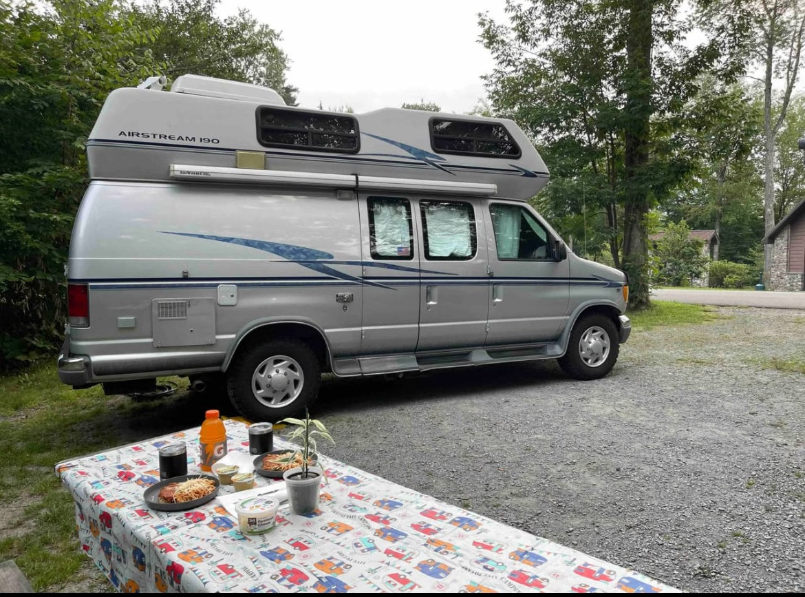 A silver Airstream 190 RV rental at a campsite with a picnic table set for a meal. Ideal for outdoor adventures and travel. — photo 5