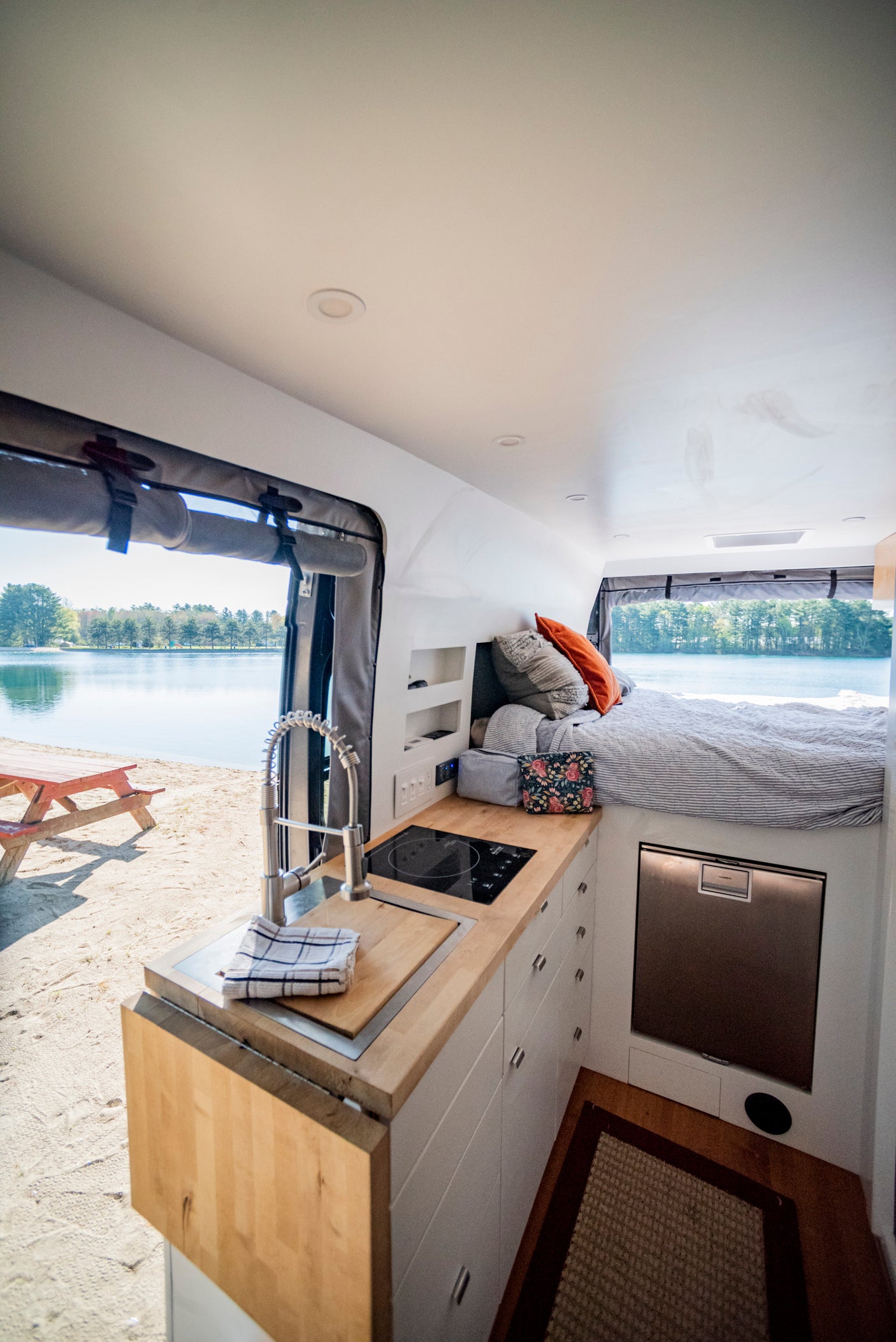 Inside a modern rv rental, featuring a full kitchen, comfortable bed, and stunning lakefront view on a sandy beach.