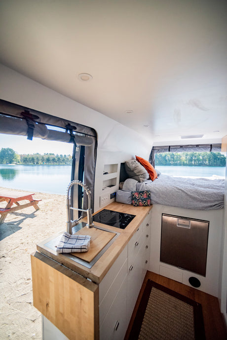 Inside a modern rv rental, featuring a full kitchen, comfortable bed, and stunning lakefront view on a sandy beach.