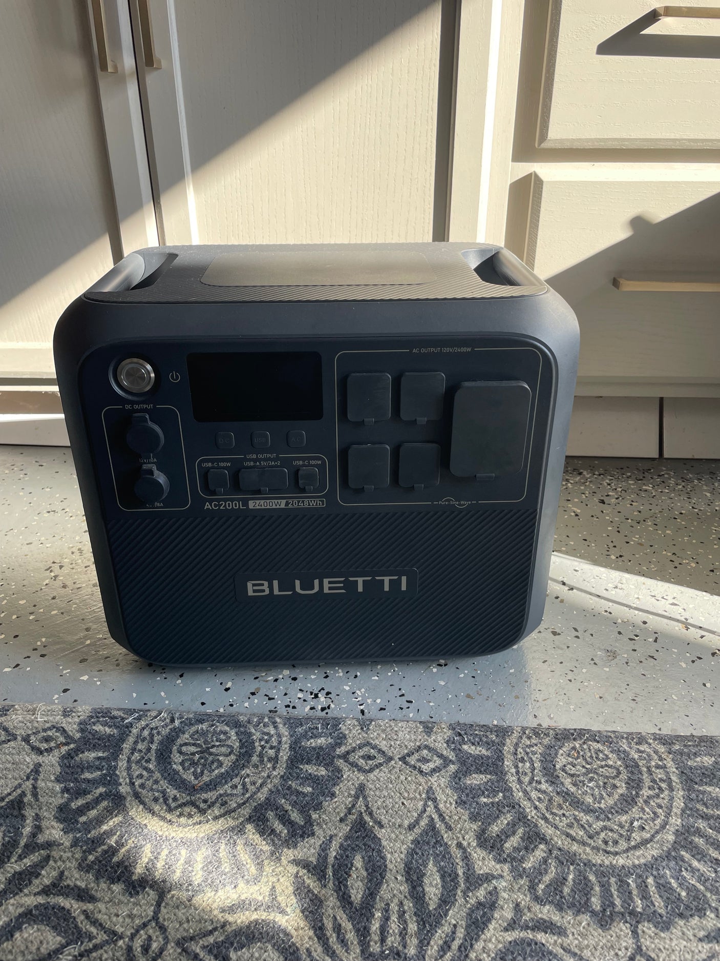 Dark gray Bluetti AC200L portable power station, great for rv rental, providing off-grid energy, on a speckled garage floor.