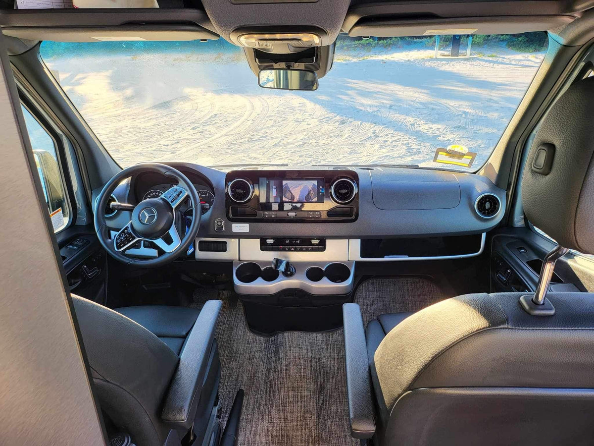 Get ready for adventure! Spacious RV rental interior shows the cockpit, steering wheel, and front seats facing a sandy road. — photo 19