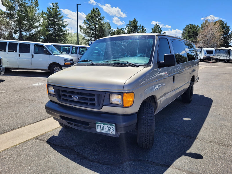 Tan Ford van parked in an RV rental lot on asphalt, with other white vans and travel trailers under a blue sky. — photo 1