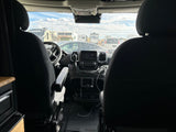 Front interior of an rv rental camper van, showing the dashboard and a view of multiple parked RVs through the windshield.