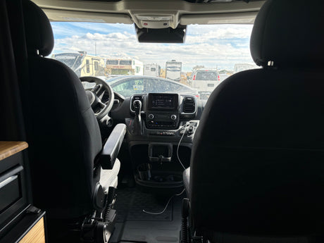 Front interior of an rv rental camper van, showing the dashboard and a view of multiple parked RVs through the windshield.